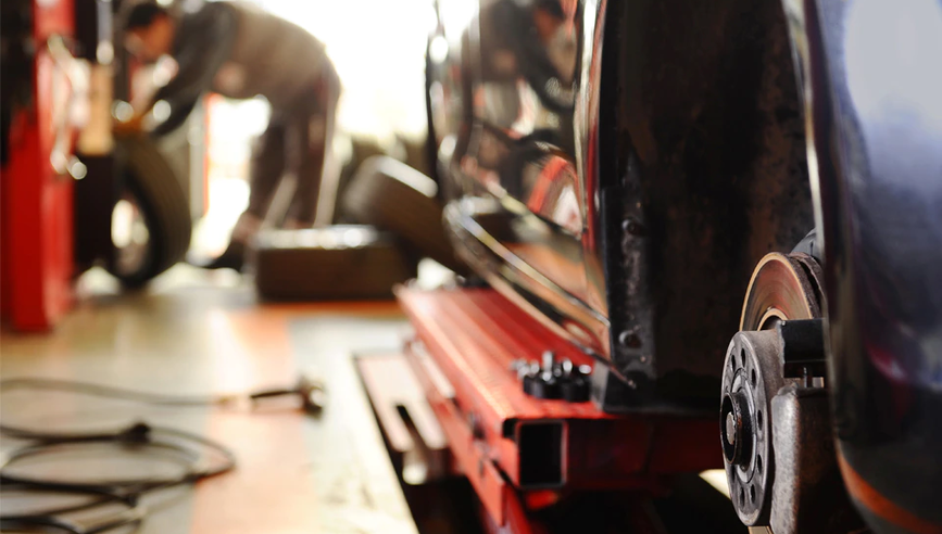 Mechanic working on car brakes in an auto body shop.