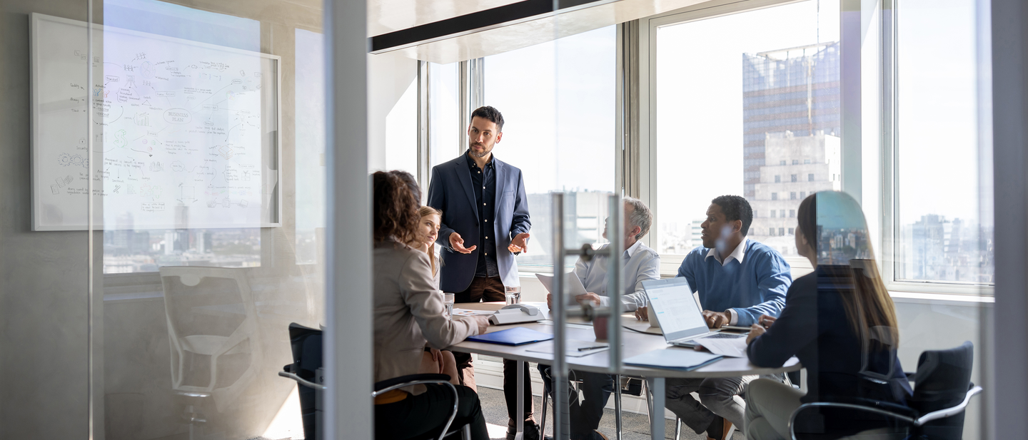 Business leaders discuss strategies in a glass conference room.