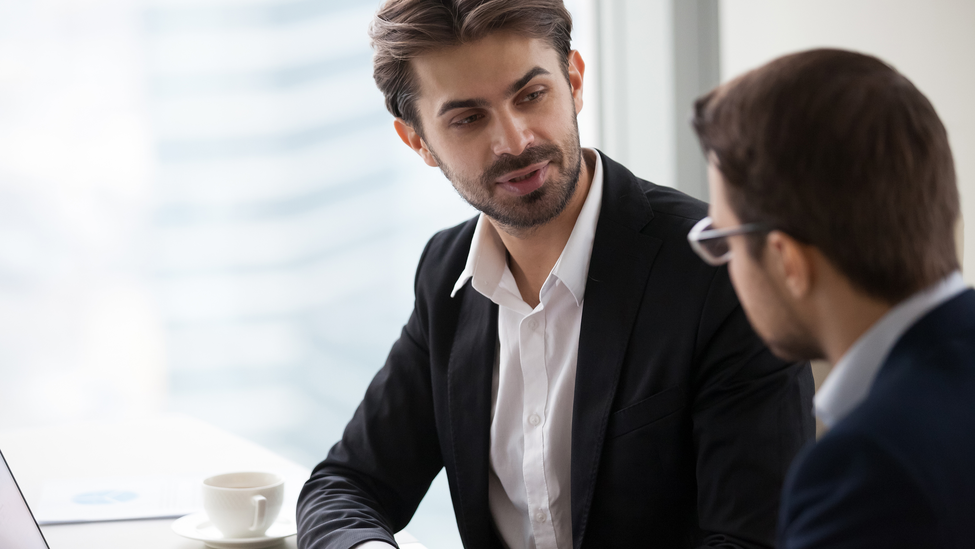 Male colleagues talking in office discussing startup project, focused businessman discuss business idea with partner, serious company CEO explaining or presenting statistics to corporate client