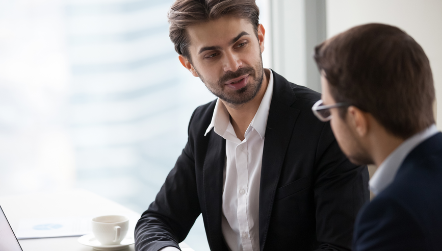 Male colleagues talking in office discussing startup project, focused businessman discuss business idea with partner, serious company CEO explaining or presenting statistics to corporate client