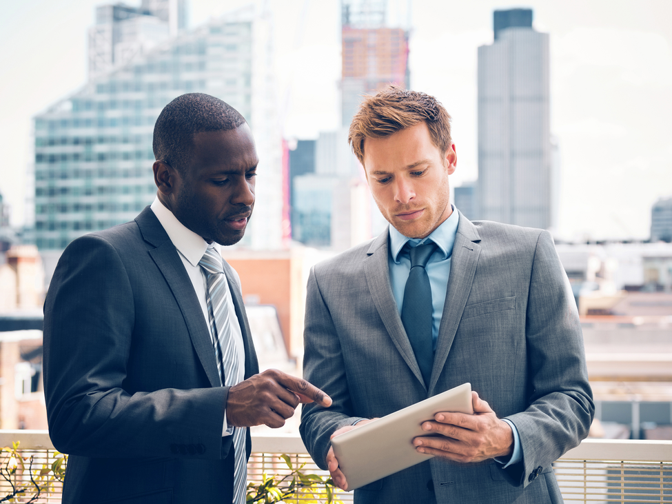 Two investors discuss a portfolio while standing on a city balcony.