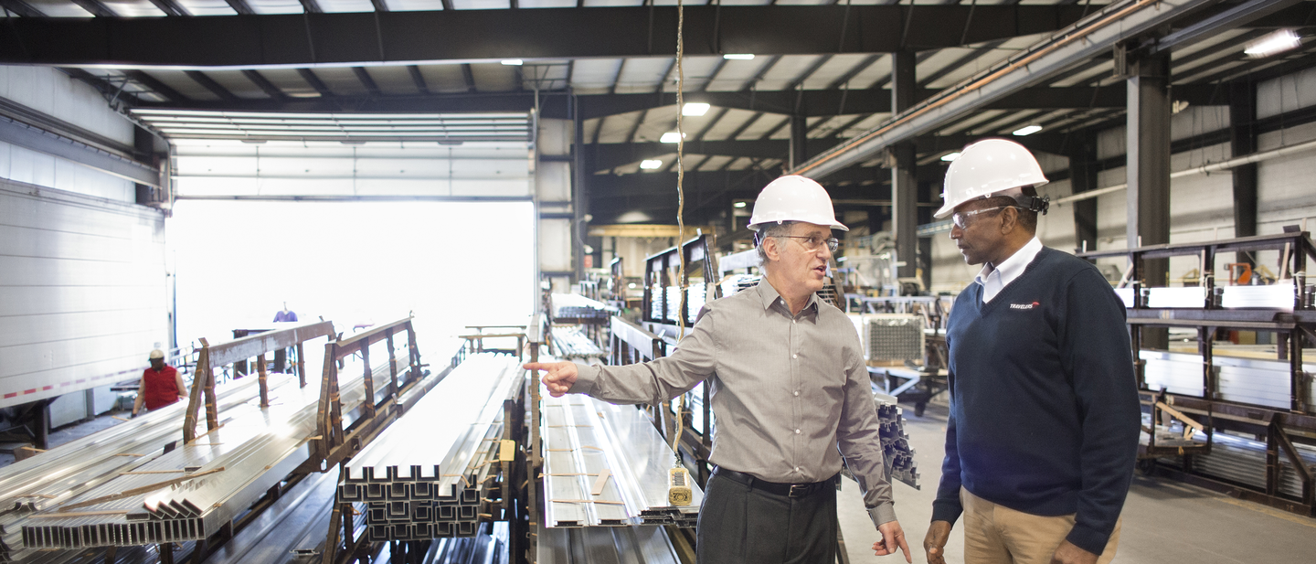 Two business people discuss manufacturing insurance in a manufacturing plant.