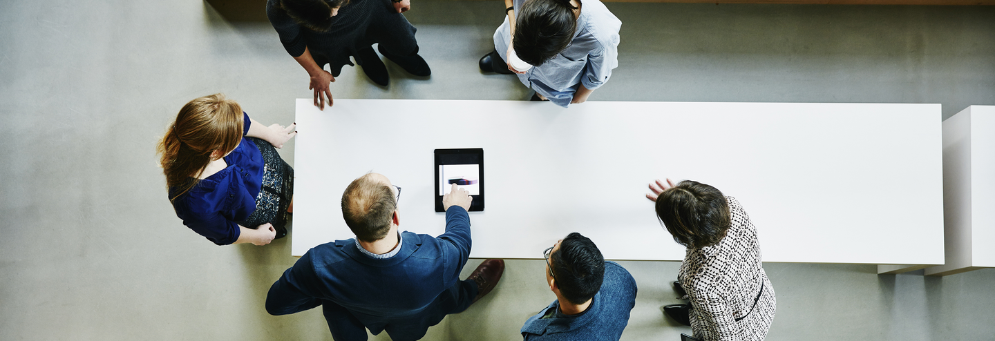 People standing around table looking at tablet.