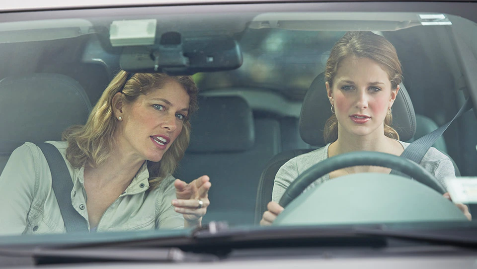 Mother instructing teen driver behind the wheel of a car.