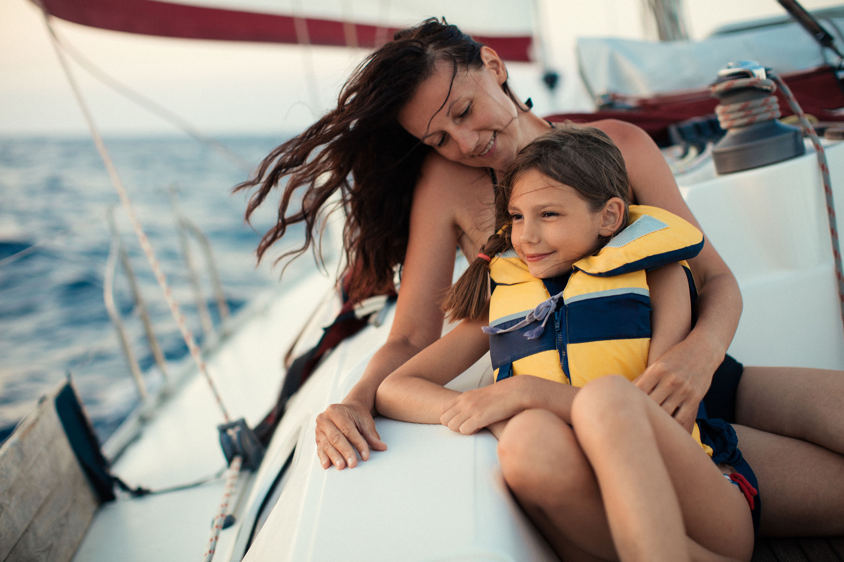Mother and child in a life vest sitting on a sailboat as it travels in the ocean.