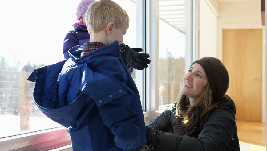 Mother zipping up son's jacket before going outside in the cold to prevent frostbite.