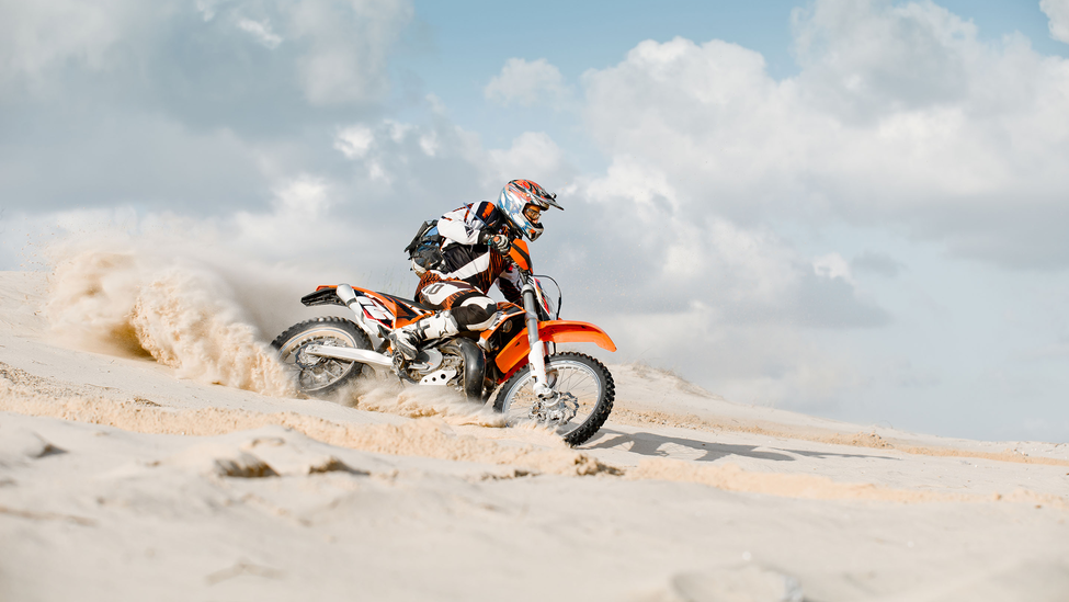 Rider making a turn in the sand on a dirt bike.