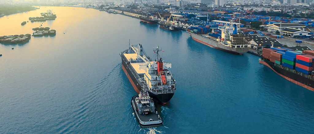 A tugboat pushing a large cargo ship near a port city.