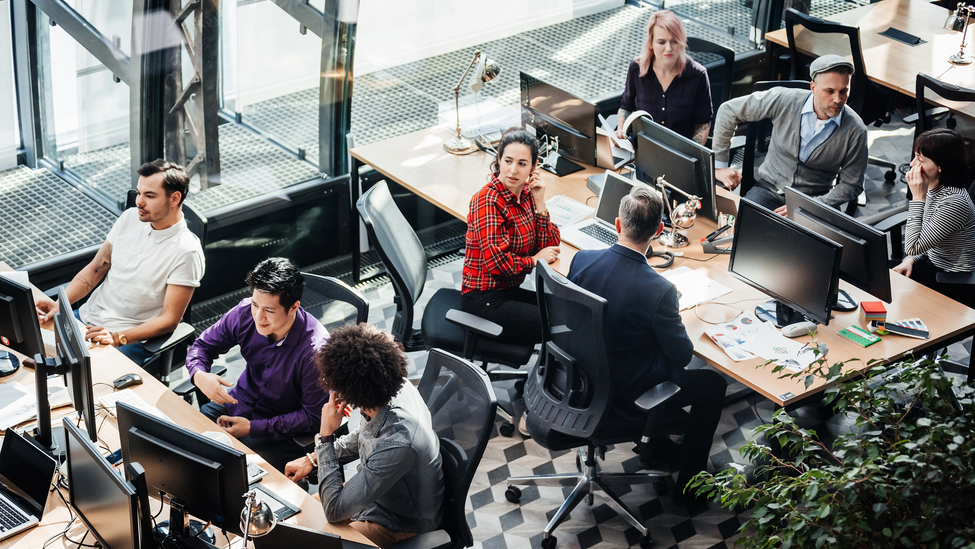 An aerial view of a modern office environment with people sitting at desks, working at computers.