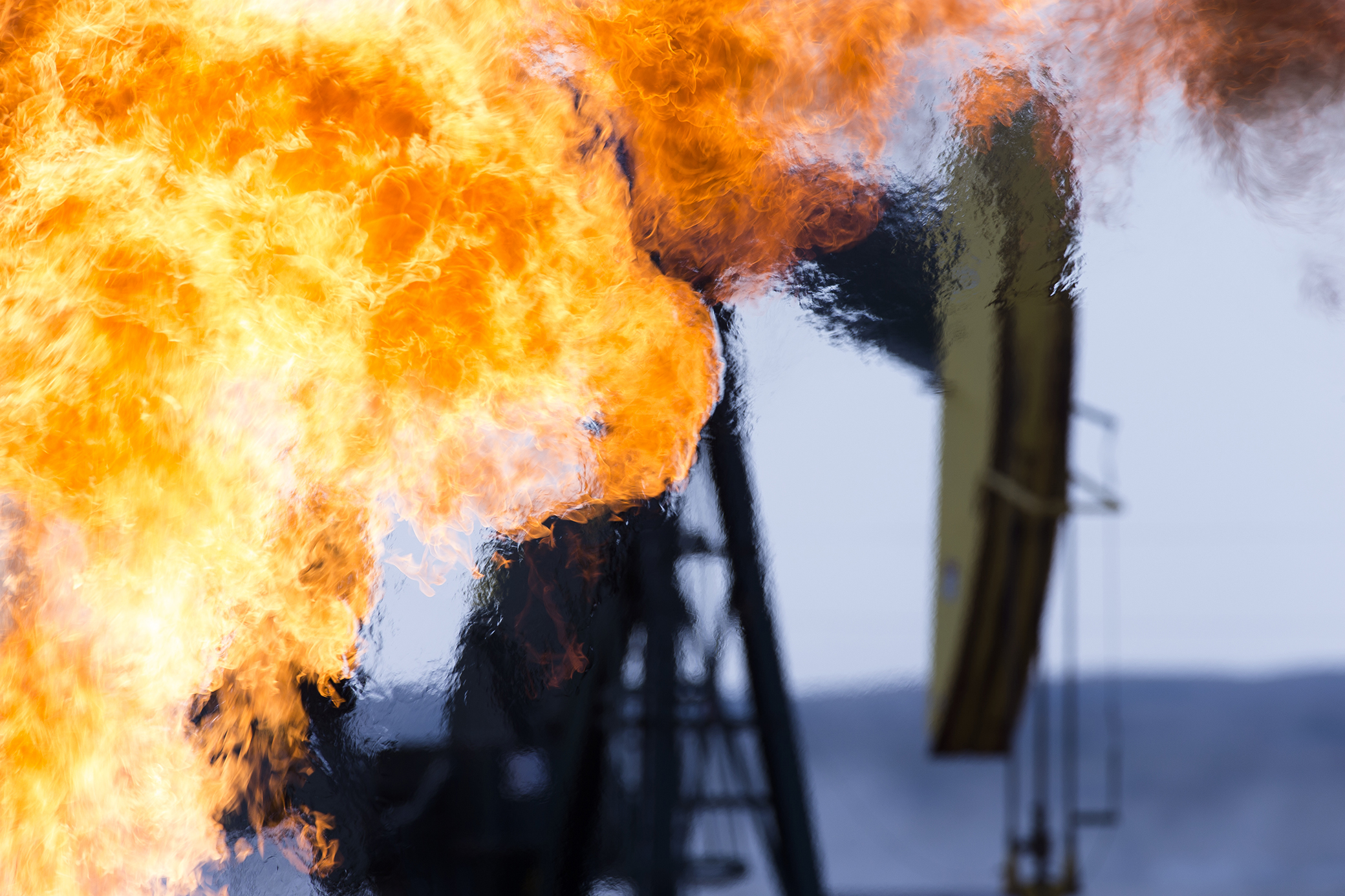 An oil well fire blazes with intense heatwavaes near a well pumpjack.