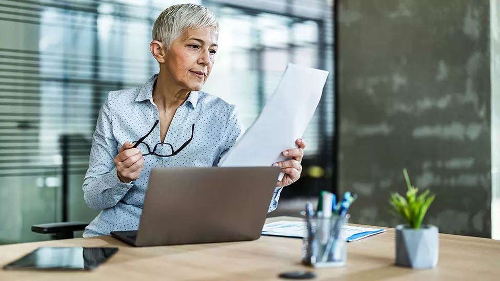 Older woman holding glasses in front of laptop reviewing commercial surety bond contract.