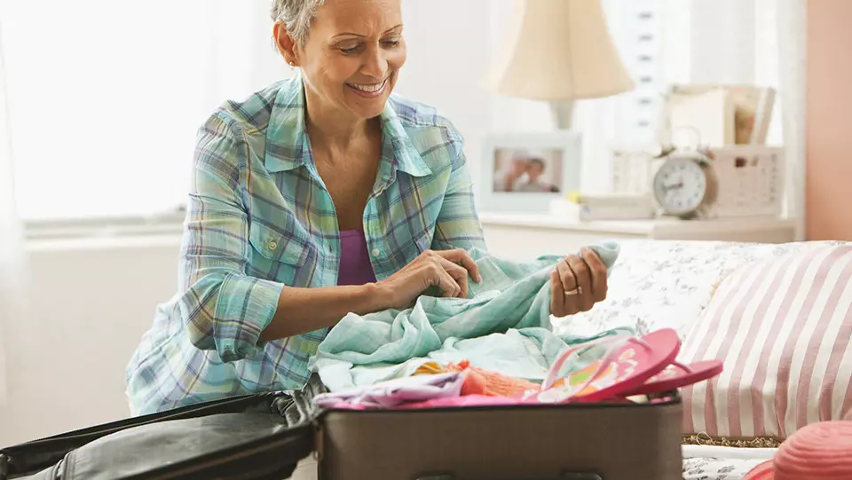 Older woman with suitcase on bed packing.