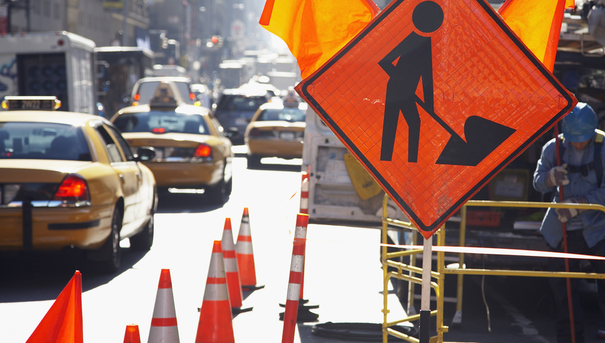 Orange construction safety sign in a busy city street.