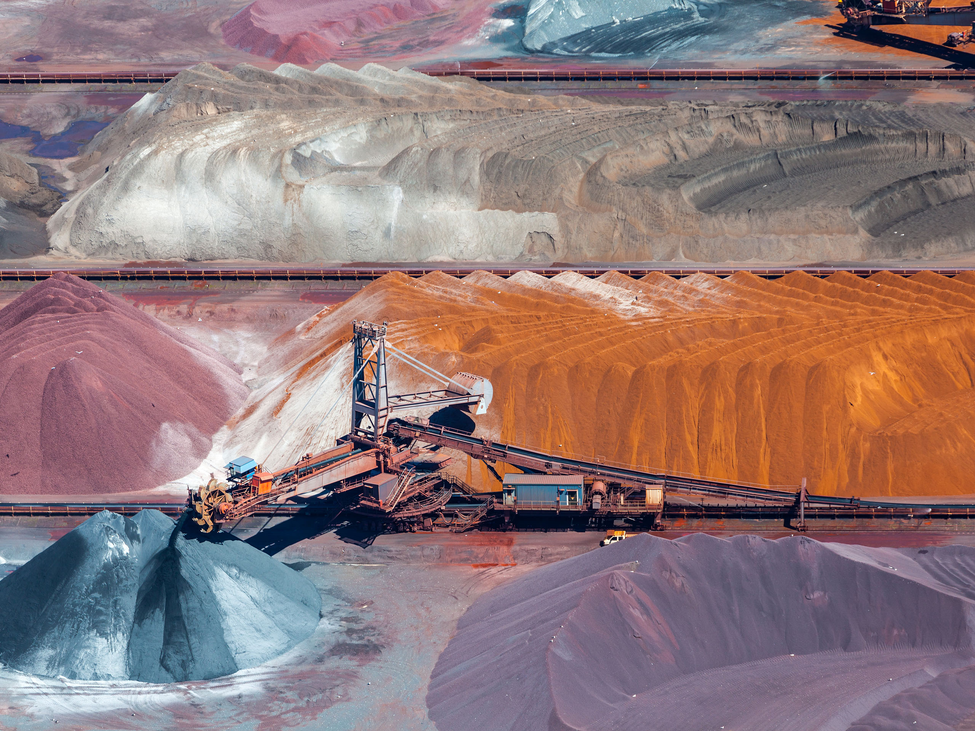 Outdoor aerial view of large ore mineral piles and a conveyor belt.