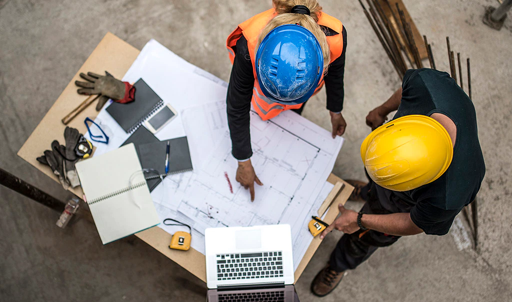 Overhead view of two construction site managers or workers studying blueprints.