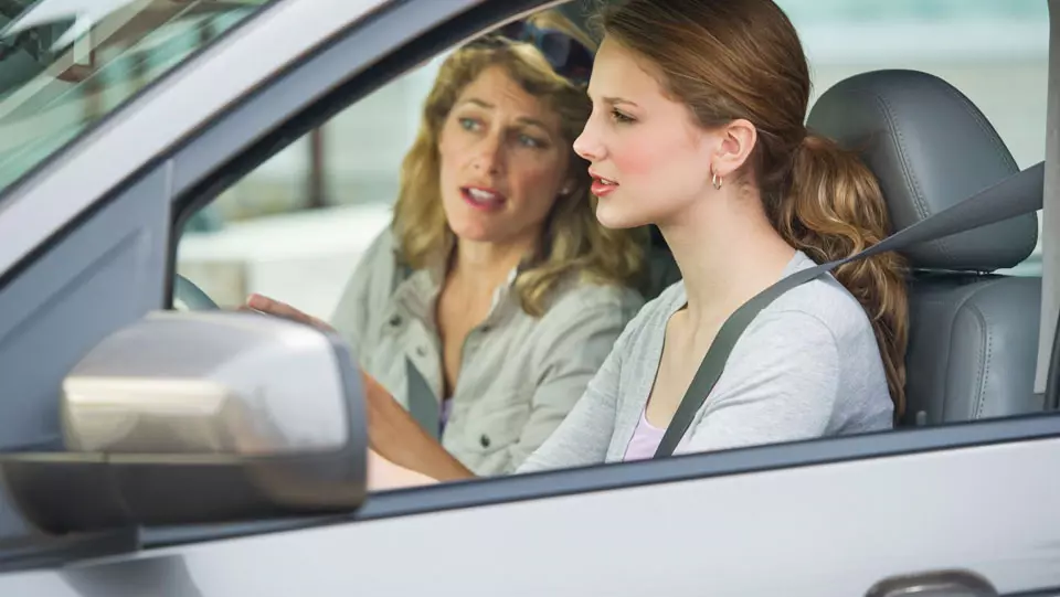 Parent teaching teen daughter how to drive.