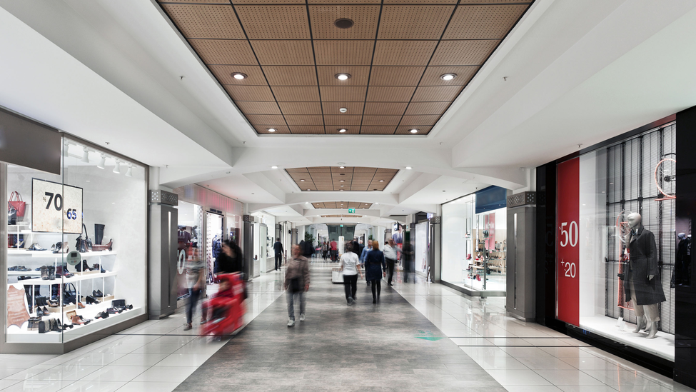 People walk inside a mall hallway with large chain retail stores on both sides. 