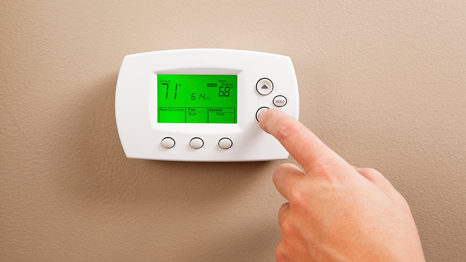 Person adjusting temperature on thermostat.