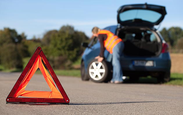 person wearing vest changing tire, with reflective triangle in the foreground