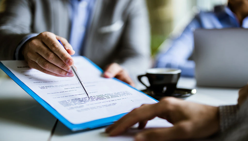 Person pointing to a contract at a meeting table.