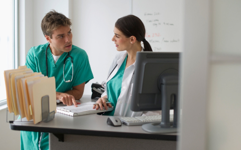 two coworkers talking together at a desk in a medical facility