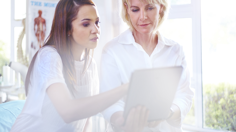 A physical therapist and a patient use a digital tablet in an examination room.