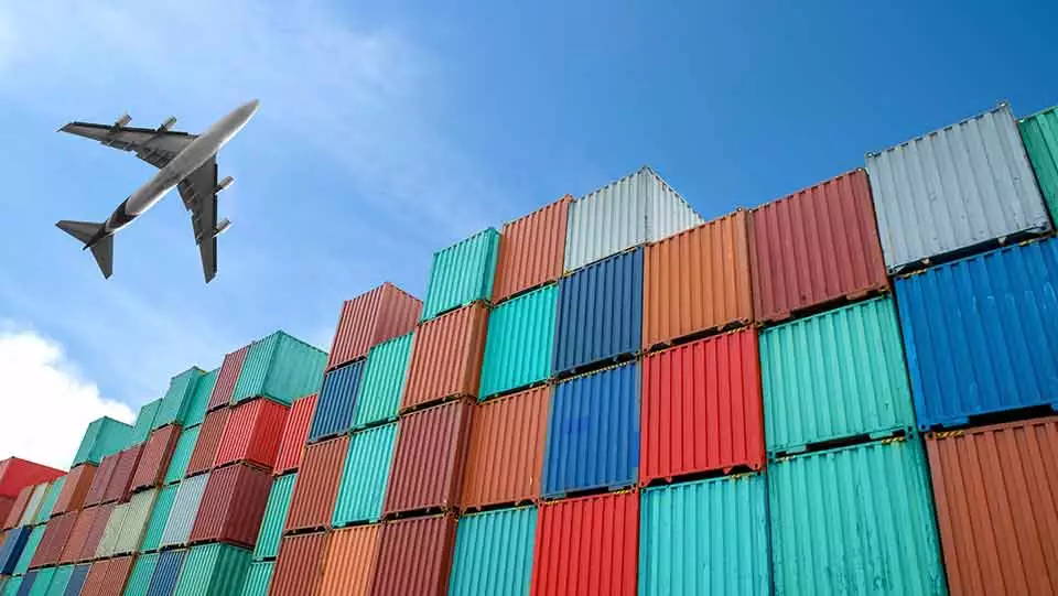 Plane flying over shipping containers in a global supply chain.
