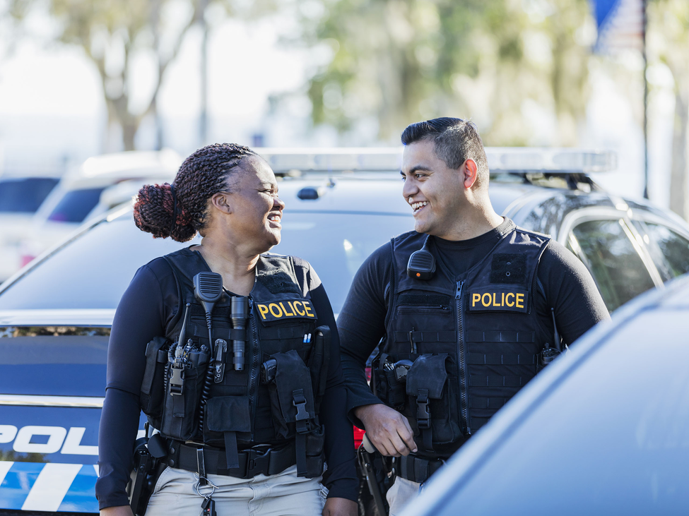 Police officers banter as they walk next to their patrol cars.