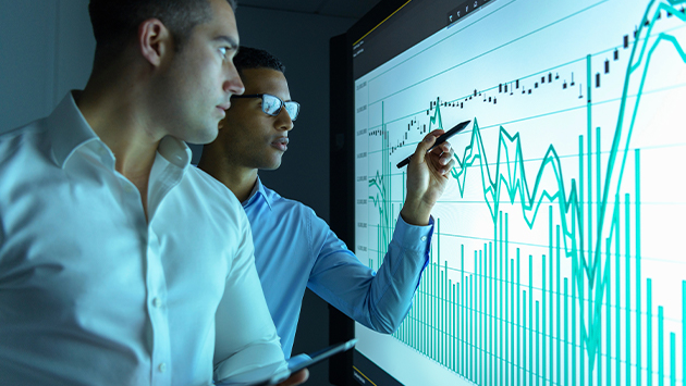 Businessmen studying graphs on an interactive screen in business meeting.