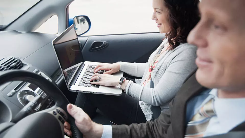 Professionals in car and passenger typing on laptop.