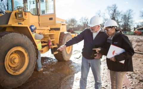 Travelers agent discussing heavy equipment with a construction worker next to a bulldozer.