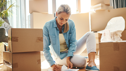 Woman surrounded by moving boxes while filling out paperwork