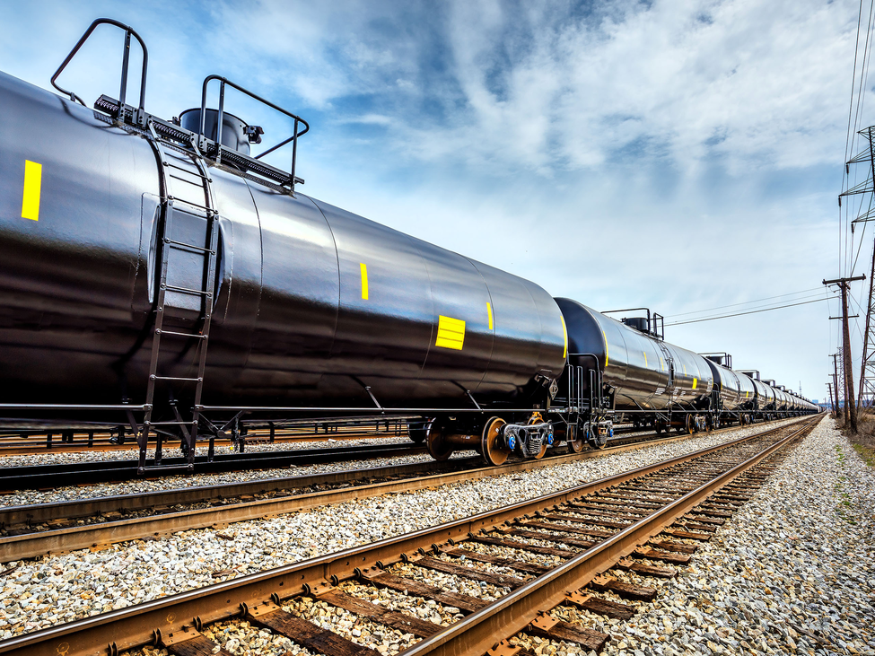Oil tanker train cars sit on a track with empty railroad tracks next to it. 