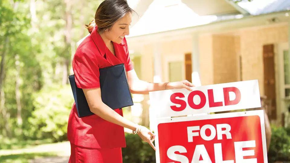 Real estate agent changing for sale sign in front of home to sold.