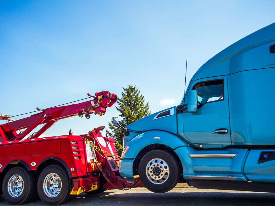Red tow truck providing roadside assistance and towing for blue truck.