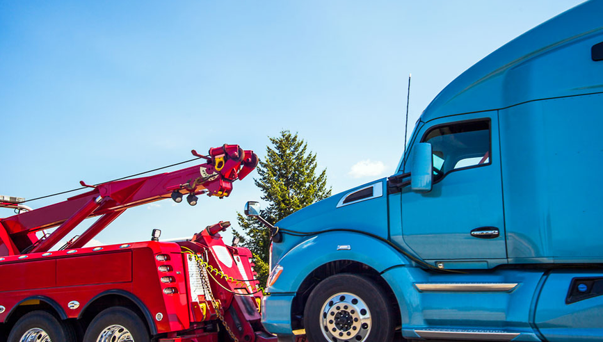 Red tow truck providing roadside assistance and towing for blue truck.