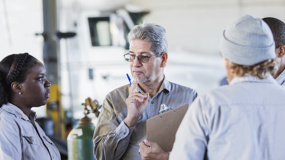 Three team members having a meeting while standing in a mechanics garage. 