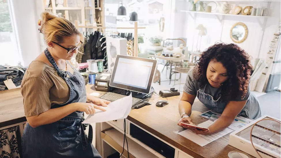 Retail employees talking looking at tablet and paperwork.