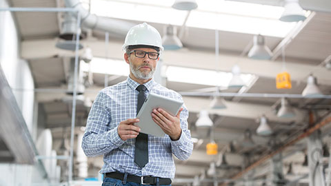 Man in hard hat with clipboard in warehouse.