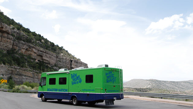 Green and blue Roadtrip Nation bus driving along a scenic road.