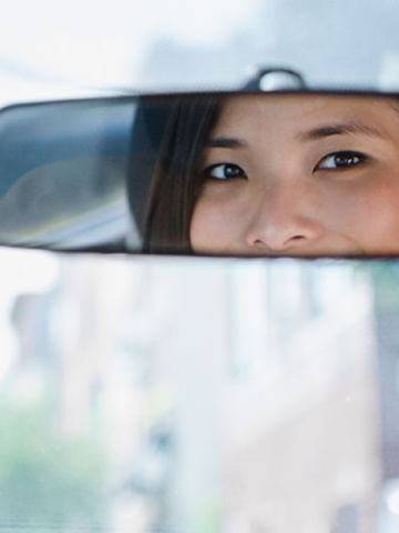 Woman looks in the rear view mirror of her car.