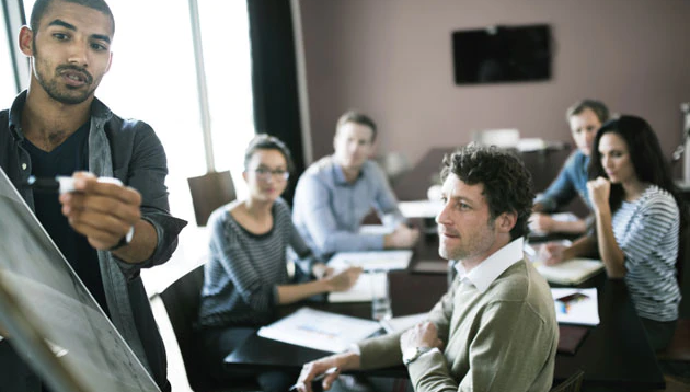 A man presenting a whiteboard in front of a group of professionals.