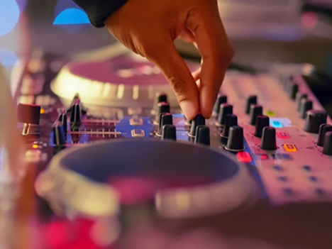 A DJ small business owner spins up music on a mixer.