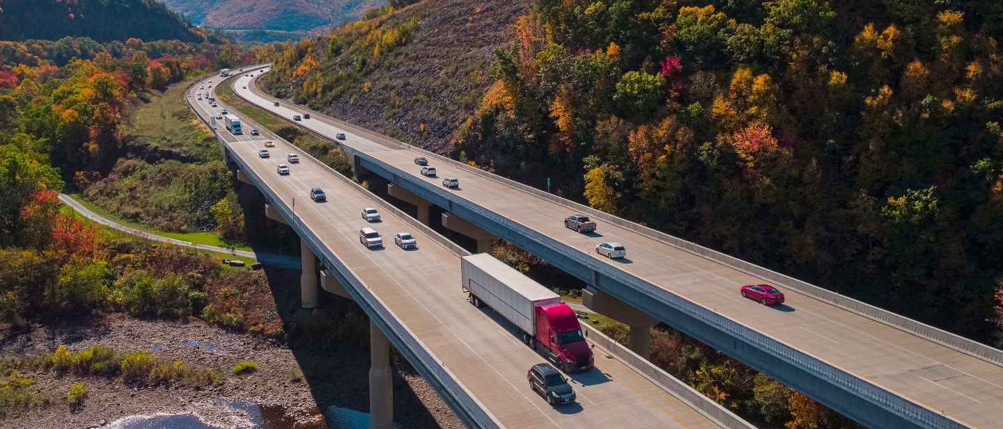 Scenic aerial view of a red and white semitruck driving on a high bridge between the mountains on a sunny fall day.