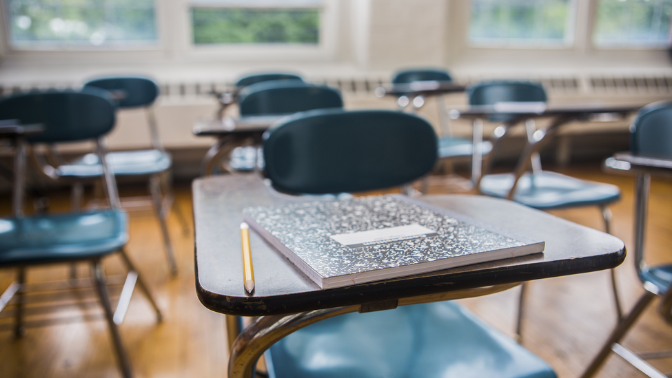 A notebook and pencil on a desk in a school classroom