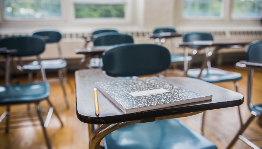 A notebook and pencil on a desk in a school classroom