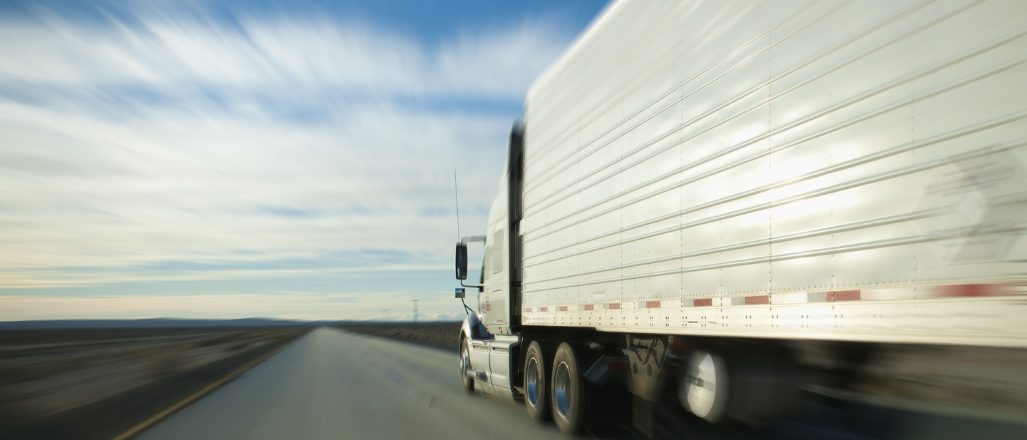 18-wheeler truck moving along flat, empty highway. 