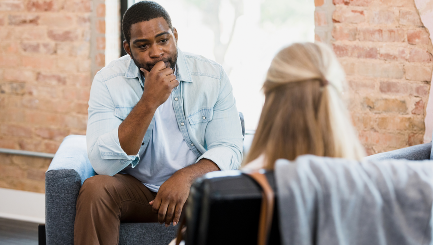 As the unrecognizable female therapist gives him advice, the exhausted mid adult man looks at her and listens.