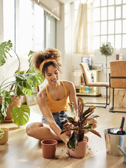 A woman is sitting on the floor of her condo repotting plants.
