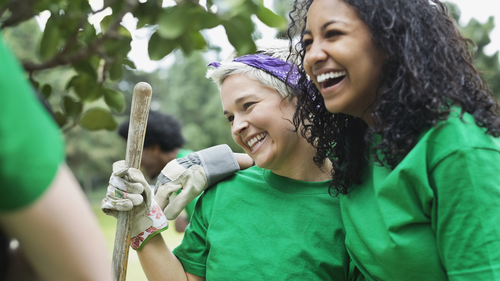 Happy young female environmentalist with friend holding shovel in park